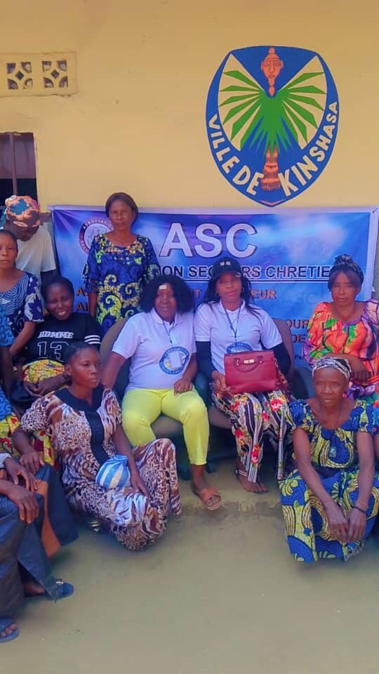 Équipe de l’Association Secours Chrétien et bénéficiaires réunies à Menkao devant l’emblème de la Ville de Kinshasa